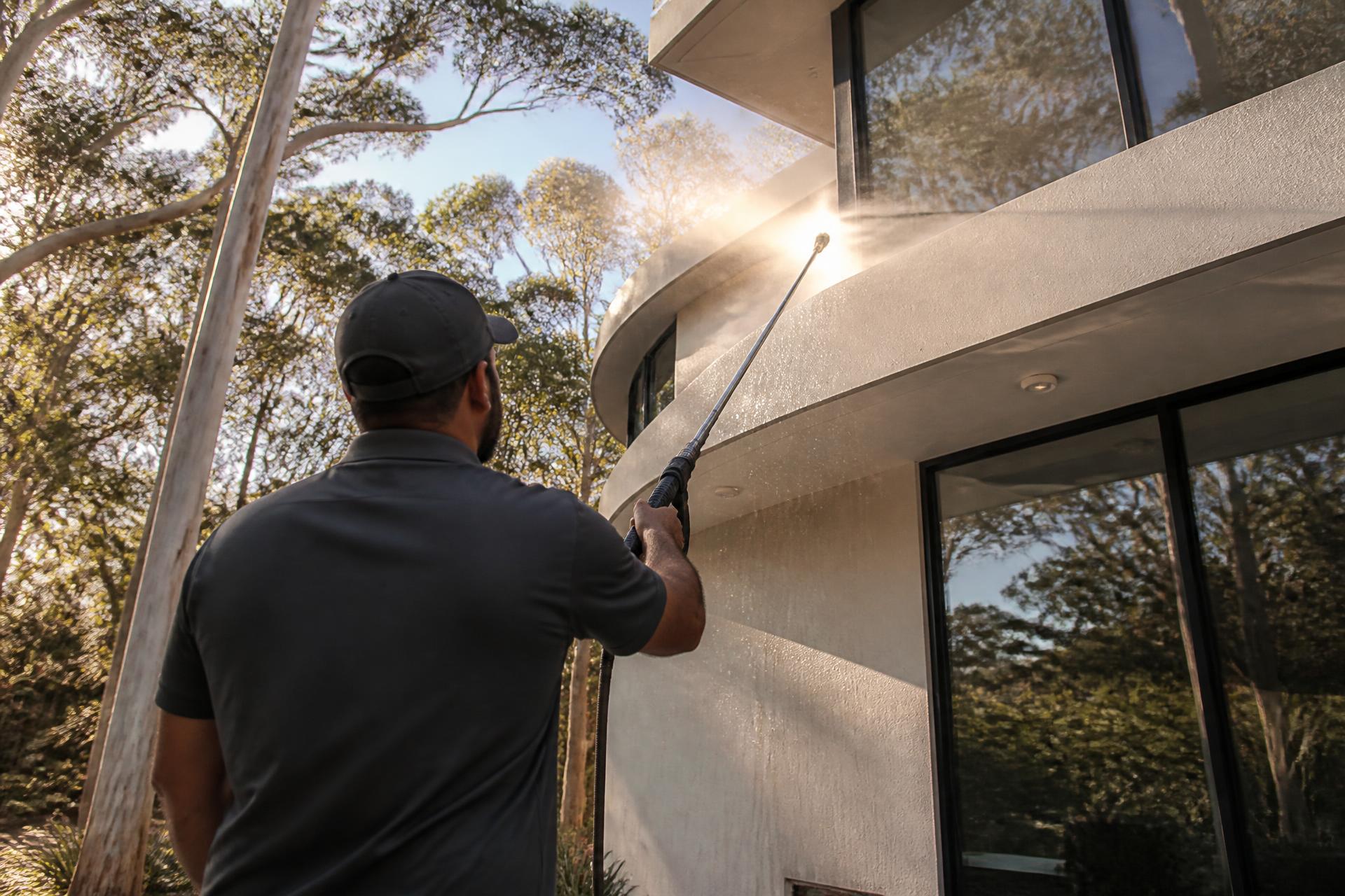 Exterior cleaning technician soft washing the render of a two-storey Sydney home